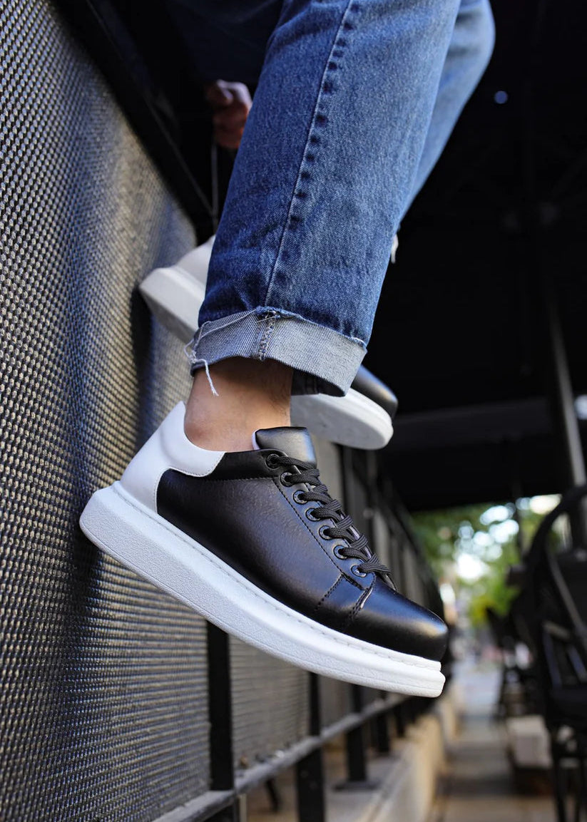 Black sneakers with white soles worn by a person, standing on a step.