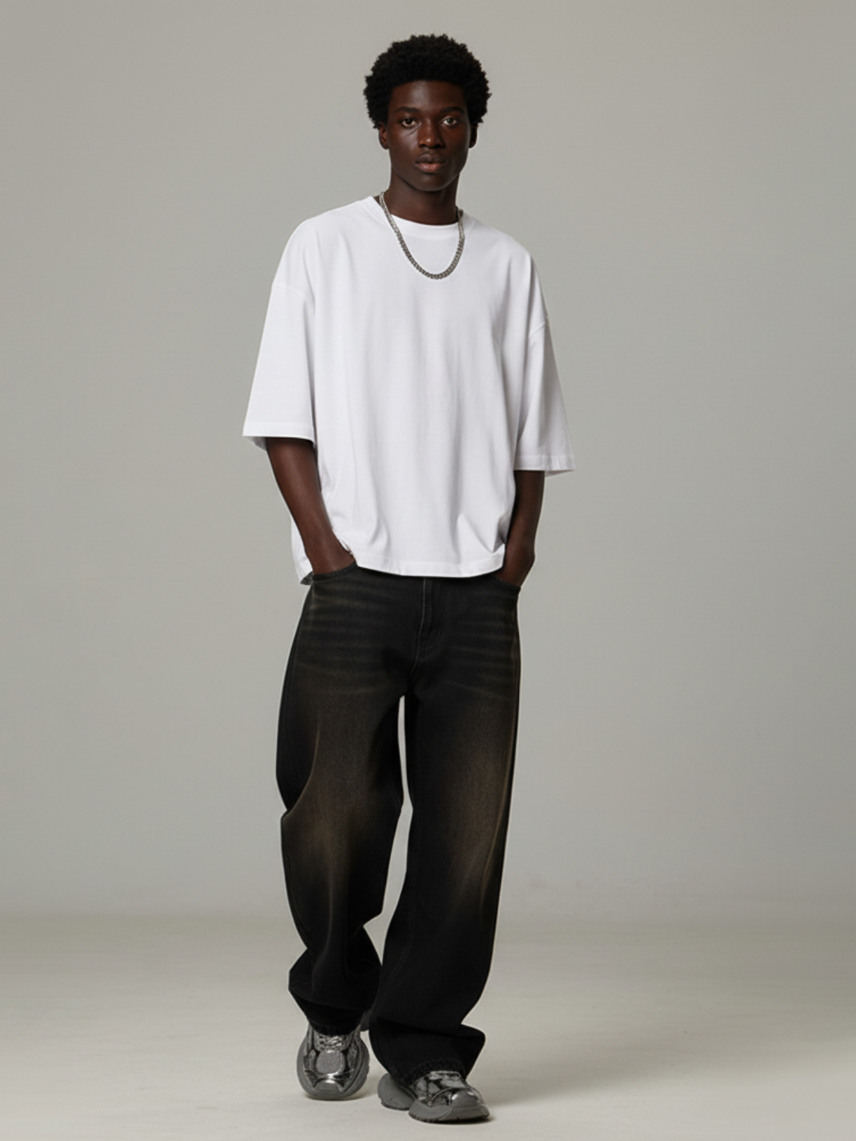 Person wearing a white oversized t-shirt and black pants on a plain background