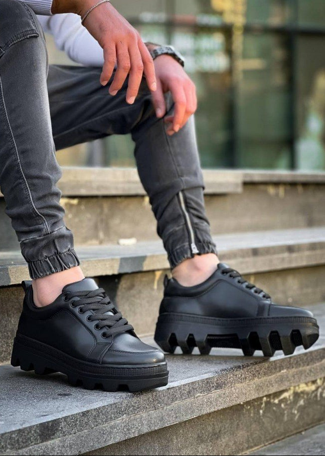 Black platform sneakers worn on a concrete surface with a blurred background