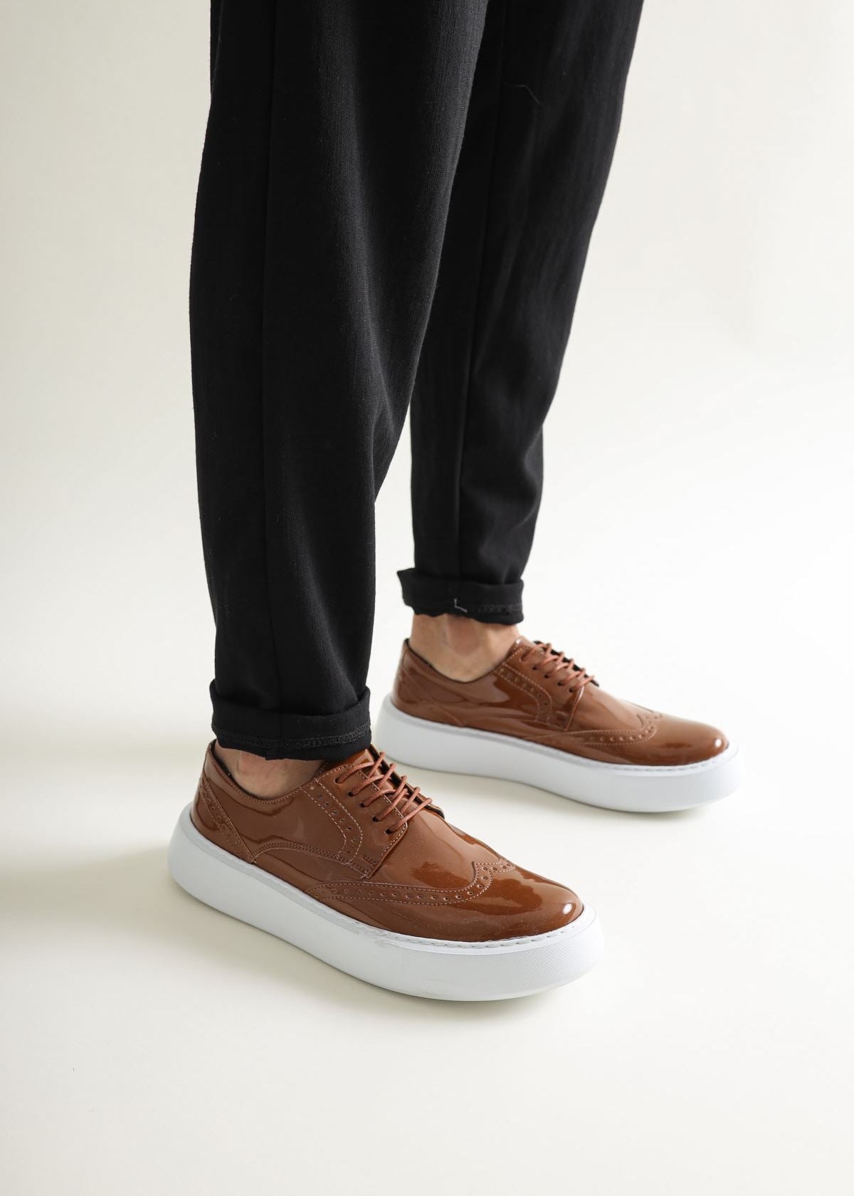 Brown leather shoes with white soles worn with black pants on a light background
