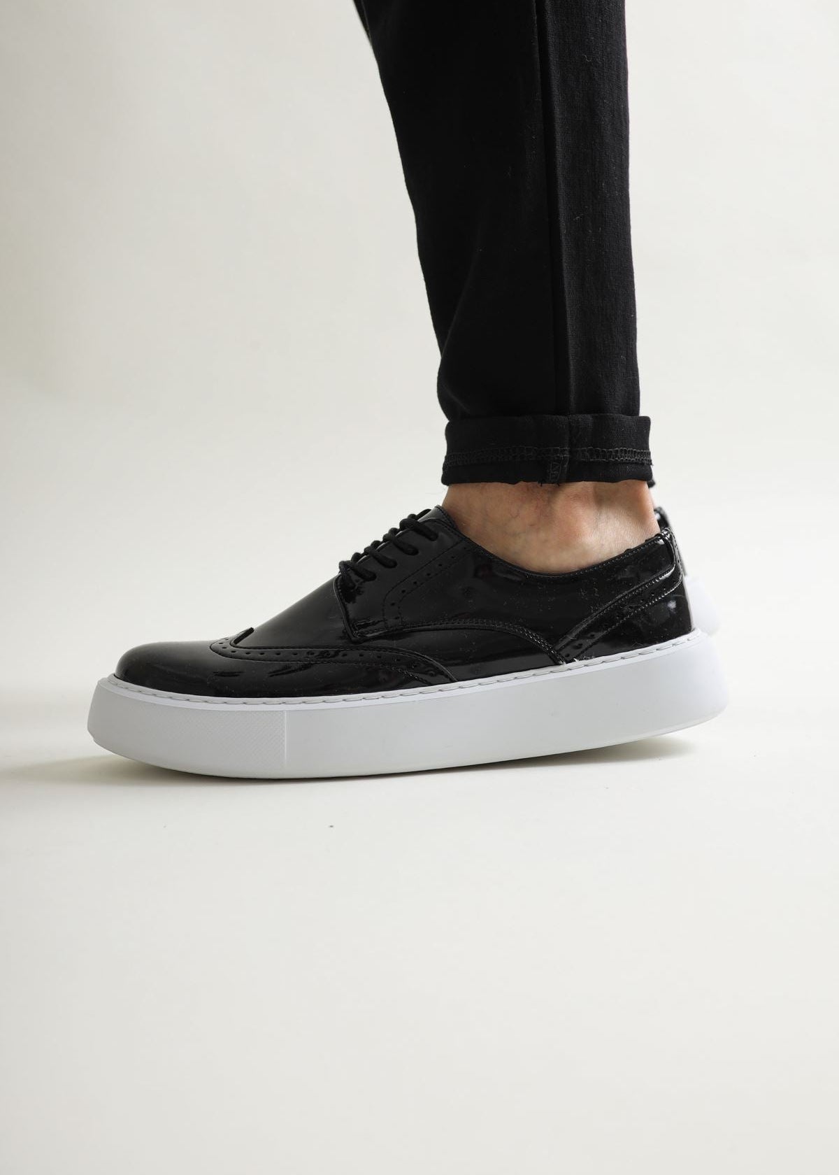 Black sneaker with white sole worn by a person on a light gray background