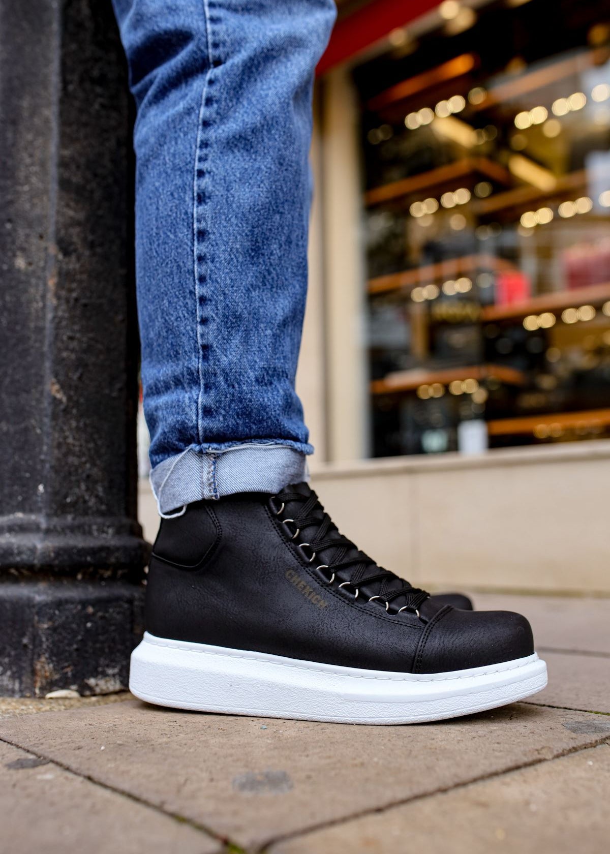 A man wearing black high-top vegan leather sneakers with white soles and blue jeans.