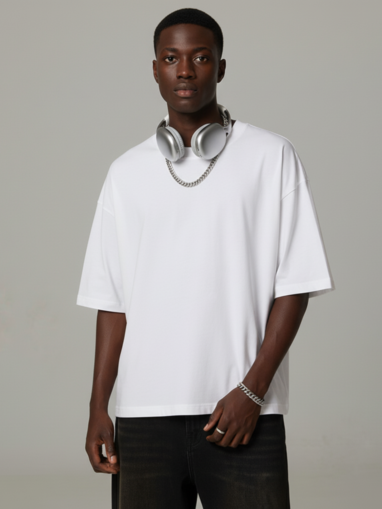 Man wearing a white t-shirt and black pants with headphones around his neck on a plain background