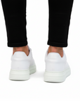White sneakers worn with black pants on a white background