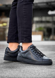Black sneakers worn with dark pants on a blurred background