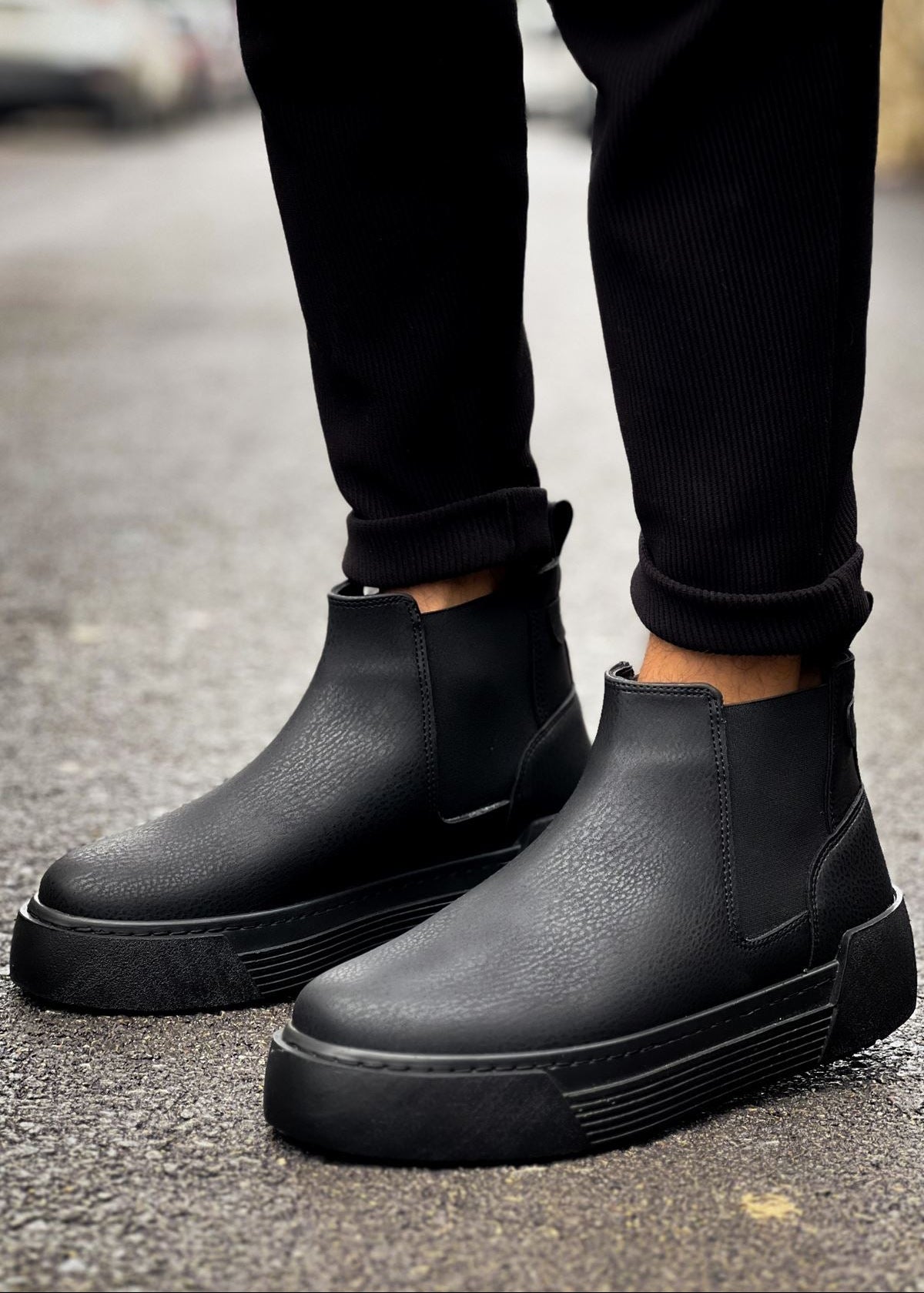 Close-up of matte black Avalon Chelsea boots worn outdoors with cuffed pants.