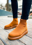 A pair of men's light brown knit ankle boots on a wooden surface, showcasing the boots' height-enhancing soles and the style of the footwear.