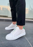 White sneakers with green accents worn on a gray pavement.